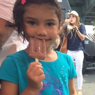 A little girl in a blue shirt is eating an ice cream bar