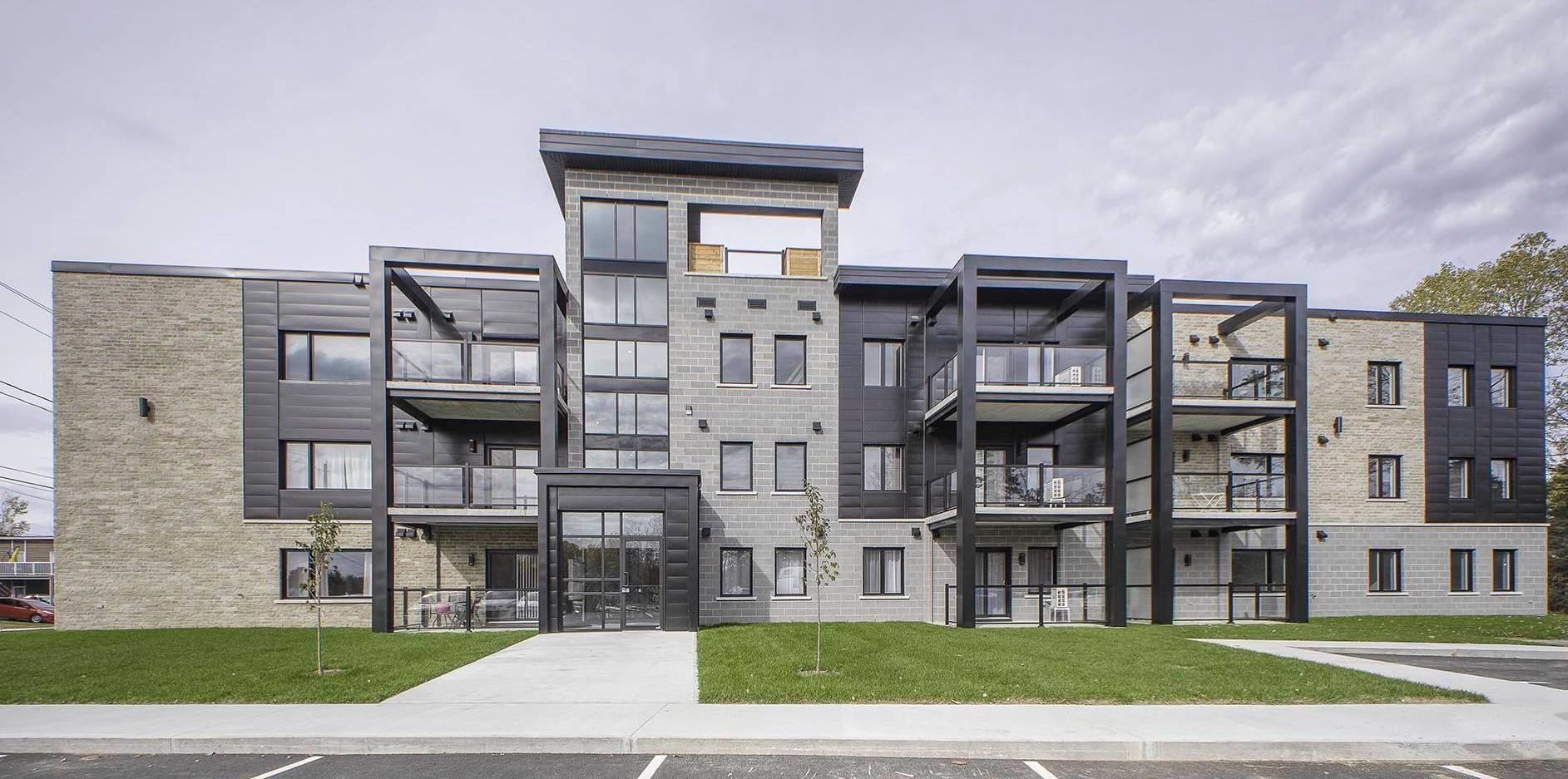 Immeuble d'appartements moderne avec pierre grise, accents noirs et balcons.