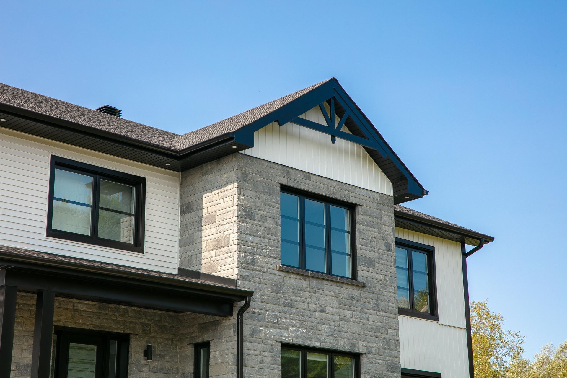 Maison à deux étages avec façade en briques et fenêtres à cadre noir sur fond de ciel bleu clair.