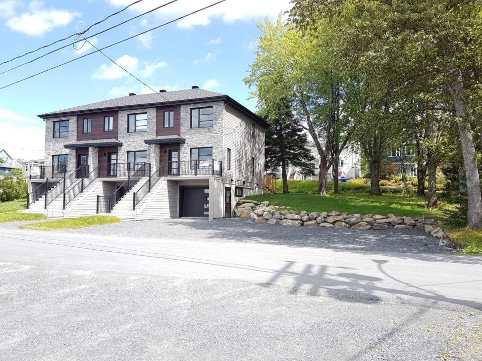 Maisons de ville avec façade en pierre grise, portes de garage noires et pelouse verte.