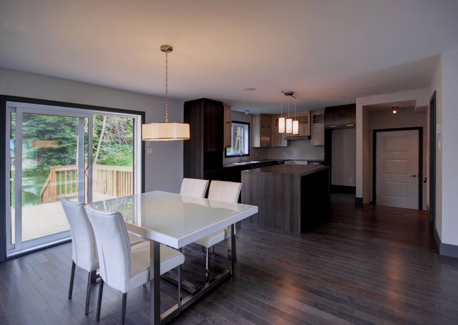 Salle à manger avec table blanche, chaises et cuisine moderne avec armoires et parquet en bois foncé.