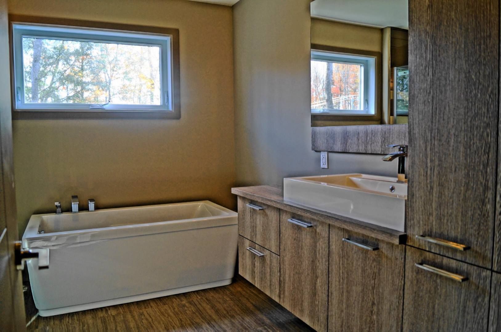 Salle de bain moderne avec baignoire, armoires en bois et grande fenêtre.