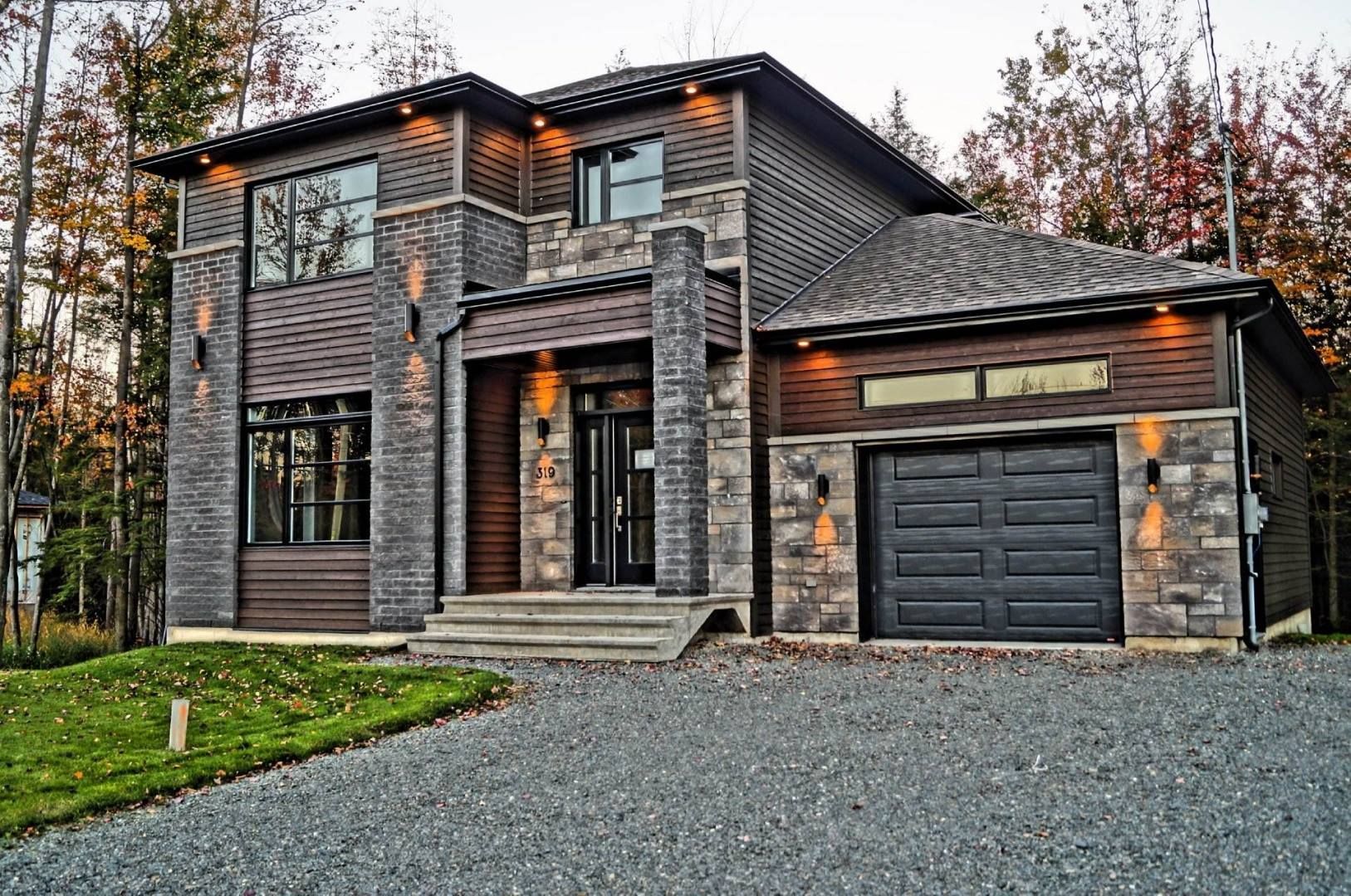 Maison moderne à deux étages avec revêtement en pierre et en bois, porte de garage noire et allée en gravier.