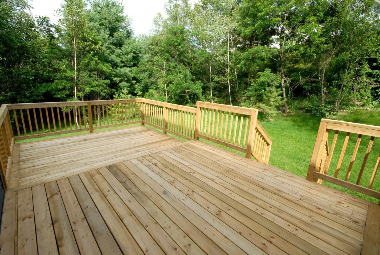 Terrasse en bois donnant sur une pelouse verte et des arbres.