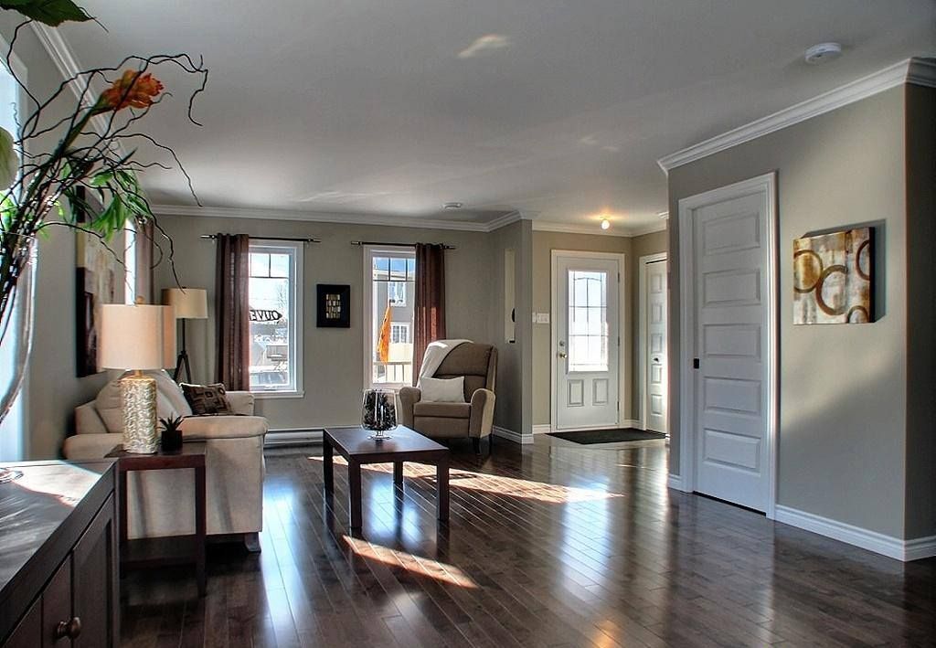 Salon spacieux avec parquet en bois foncé, murs neutres et lumière naturelle. Meublé avec canapé, chaises, table basse et décoration.