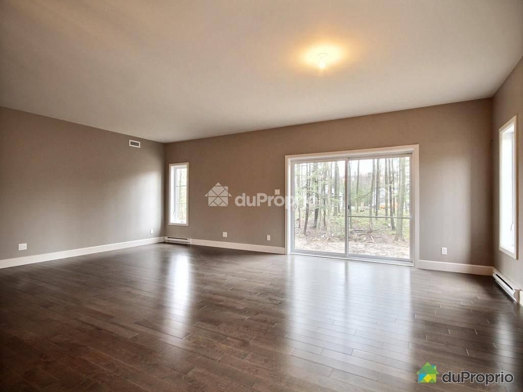Salon vide avec murs marron et parquet; porte coulissante en verre vers l'extérieur.