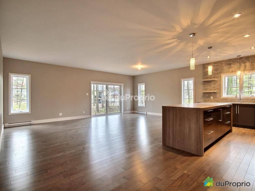 Espace de vie à aire ouverte avec planchers de bois, îlot de cuisine moderne et porte coulissante en verre vers l'extérieur.