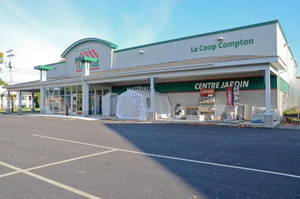 Bâtiment La Coop Compton avec jardinerie. Vue extérieure avec touches de vert et de blanc et stationnement.