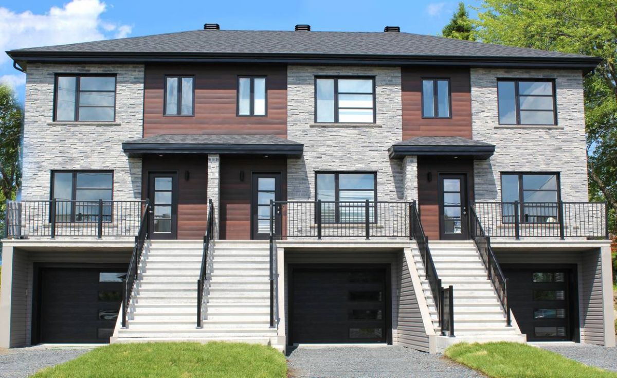 Trois maisons de ville modernes avec façade en briques, fenêtres et portes sombres et portes de garage noires.