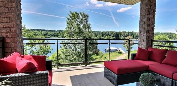 Terrasse extérieure avec mobilier rouge, vue sur un lac, un quai et des arbres verts. Ciel bleu.