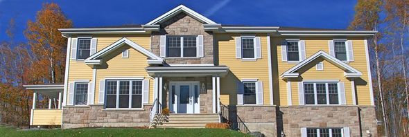 Maison jaune à deux étages avec des accents de pierre et un ciel bleu.
