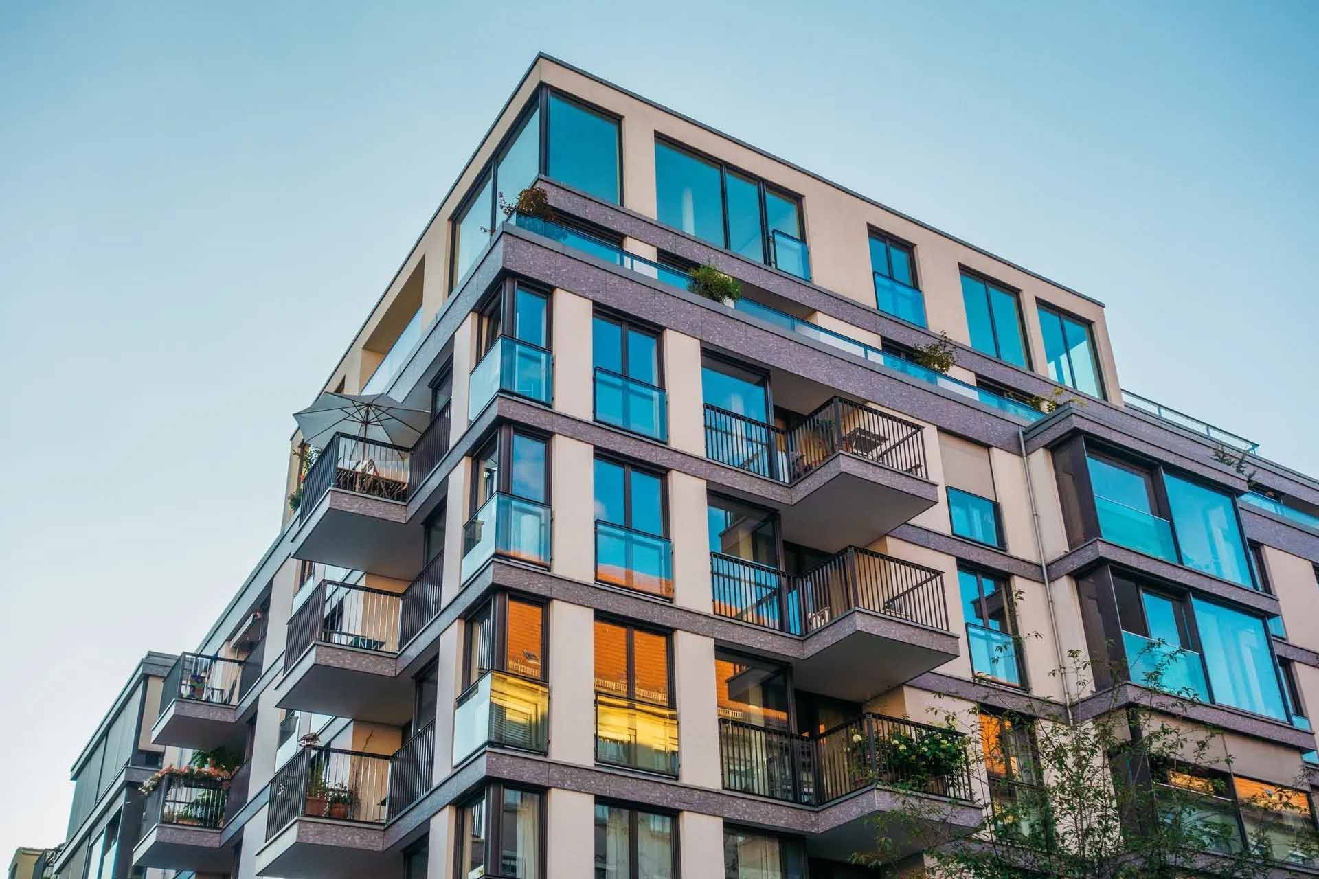 Immeuble d'appartements moderne avec balcons et grandes fenêtres contre un ciel bleu.