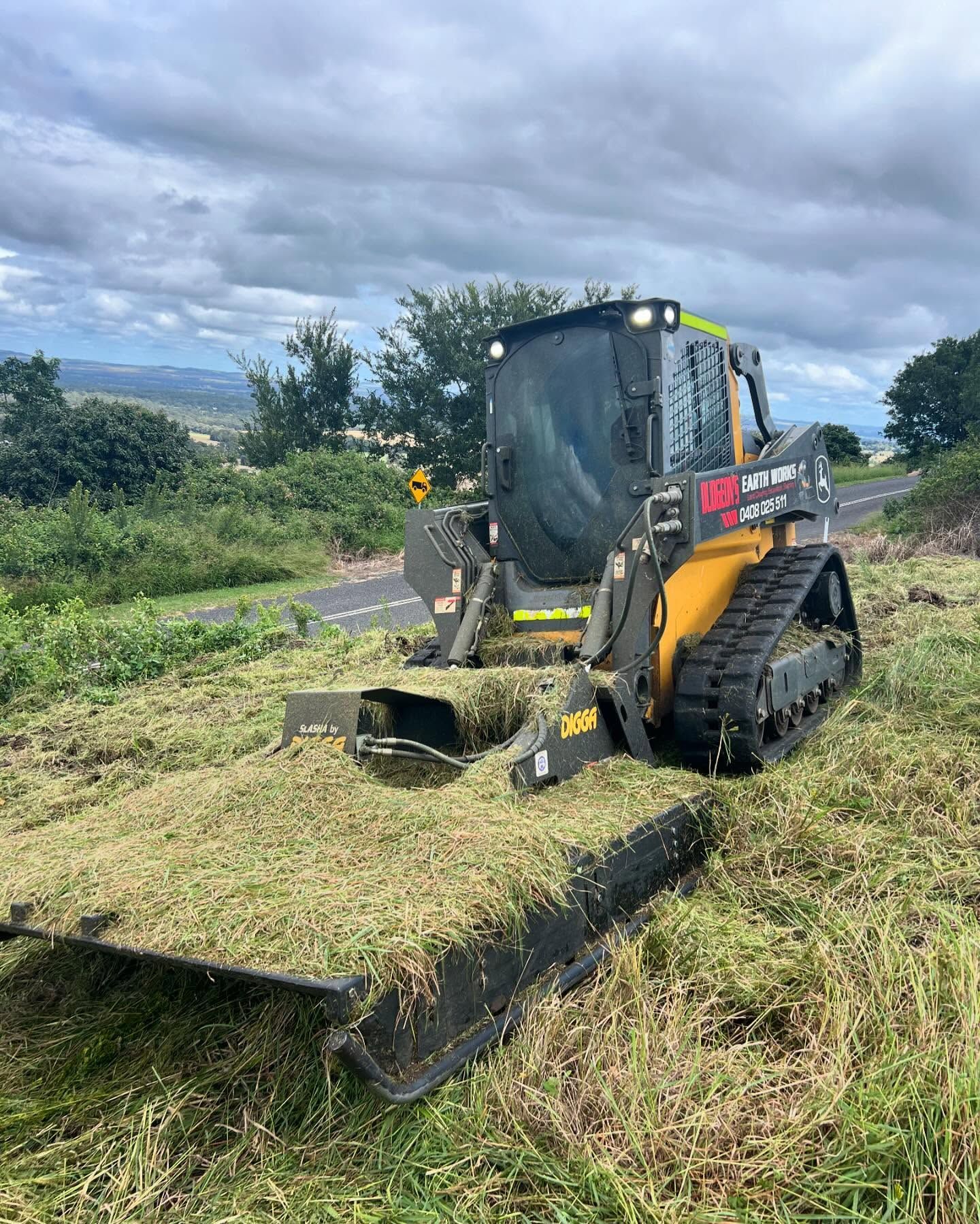 Yellow and Black Track Loader With Mower Attachment Cutting Roadside Grass — Dudgeon’s Earthworks in Murgon, QLD