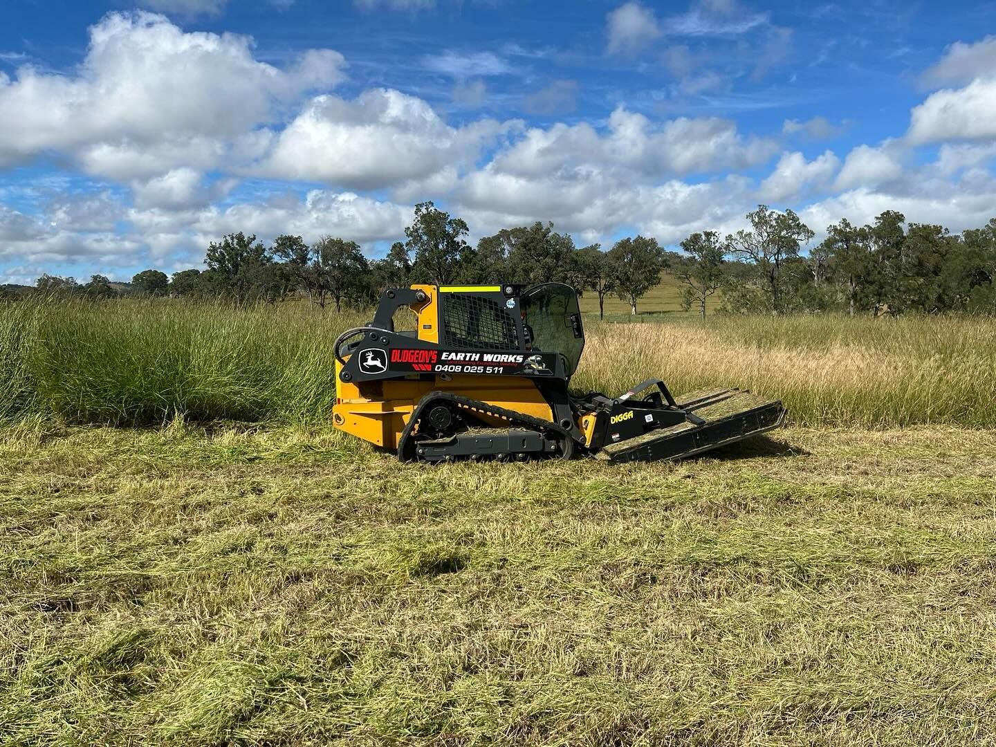 Yellow and Black Tracked Brush Cutter Mowing Tall Grass in a Field Under a Cloudy Sky — Dudgeon’s Earthworks in Murgon, QLD