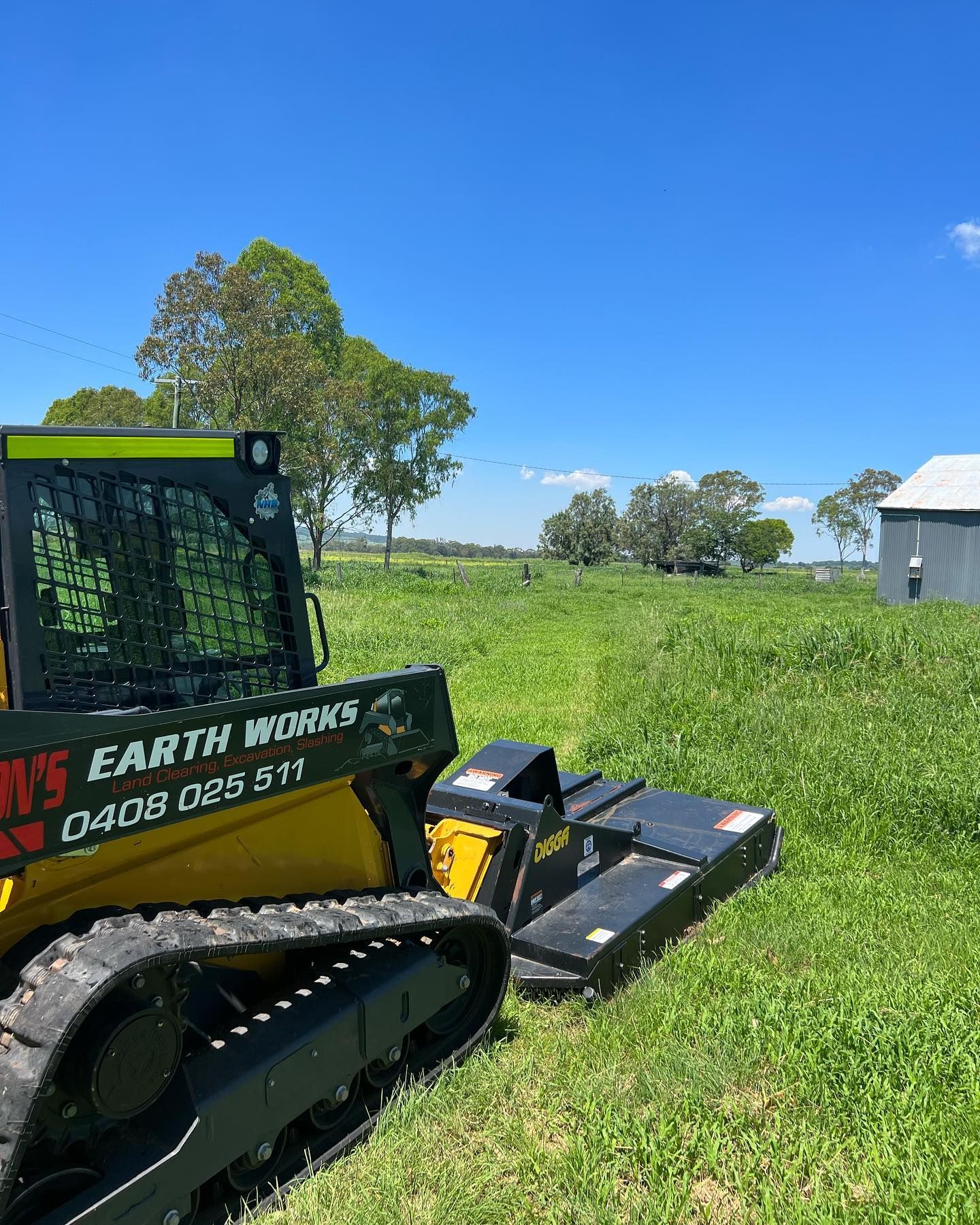 Yellow and Black Skid Steer Mower Cutting Grass in a Field Under a Blue Sky — Dudgeon’s Earthworks in Murgon, QLD