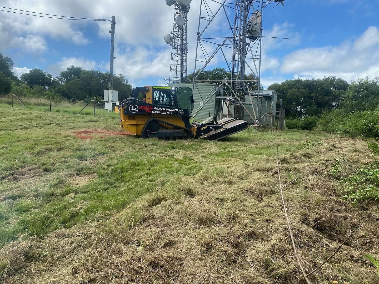 Yellow Skid-steer With Brush Cutter Mowing Grass Near a Telecommunications Tower — Dudgeon’s Earthworks in Murgon, QLD
