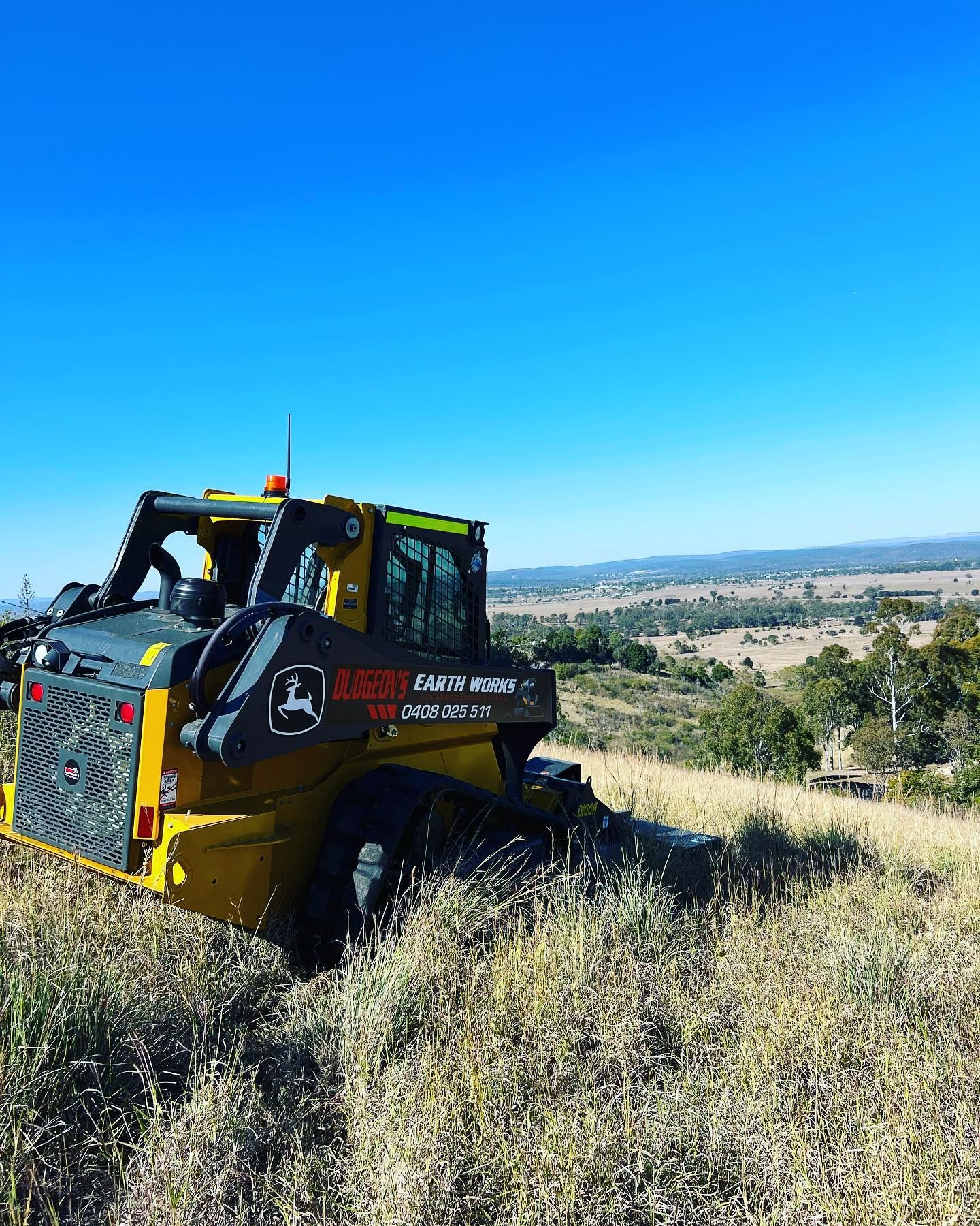 Yellow John Deere Skid Steer Tractor on a Grassy Hill, Overlooking a Valley — Dudgeon’s Earthworks in Murgon, QLD