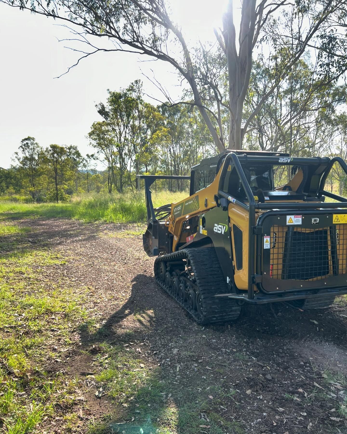 Yellow Tracked Skid Steer on a Dirt Path, Trees and Green Foliage in the Background — Dudgeon’s Earthworks in Murgon, QLD