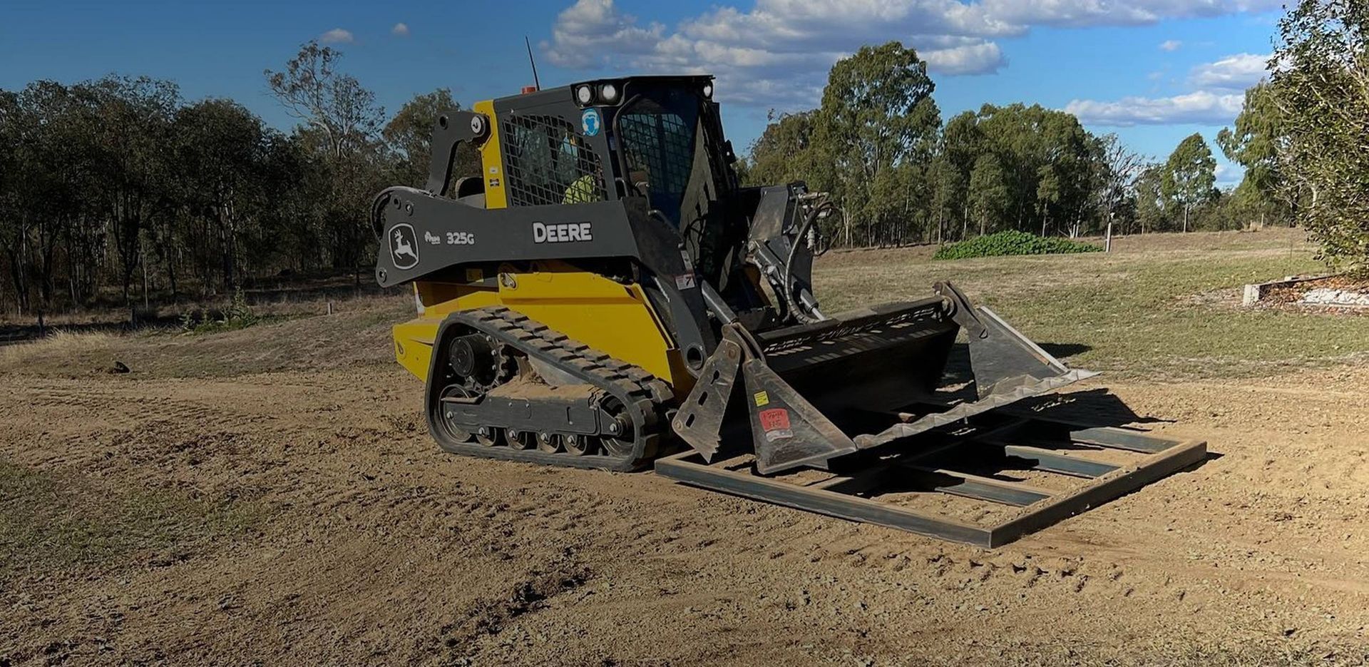 Yellow and Black Track Loader Clearing a Dirt Field, Sunny Day, Trees in Background — Dudgeon’s Earthworks in Murgon, QLD