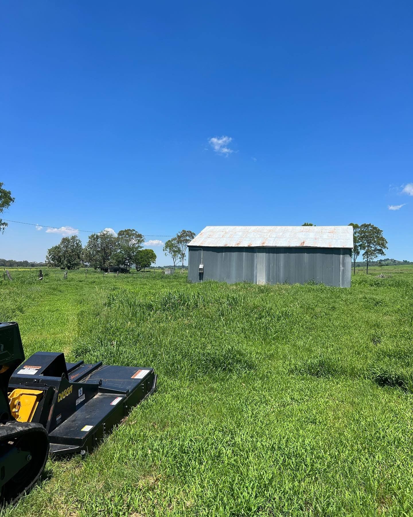 Field With Tall Green Grass and a Gray Metal Building Under a Blue Sky — Dudgeon’s Earthworks in Murgon, QLD