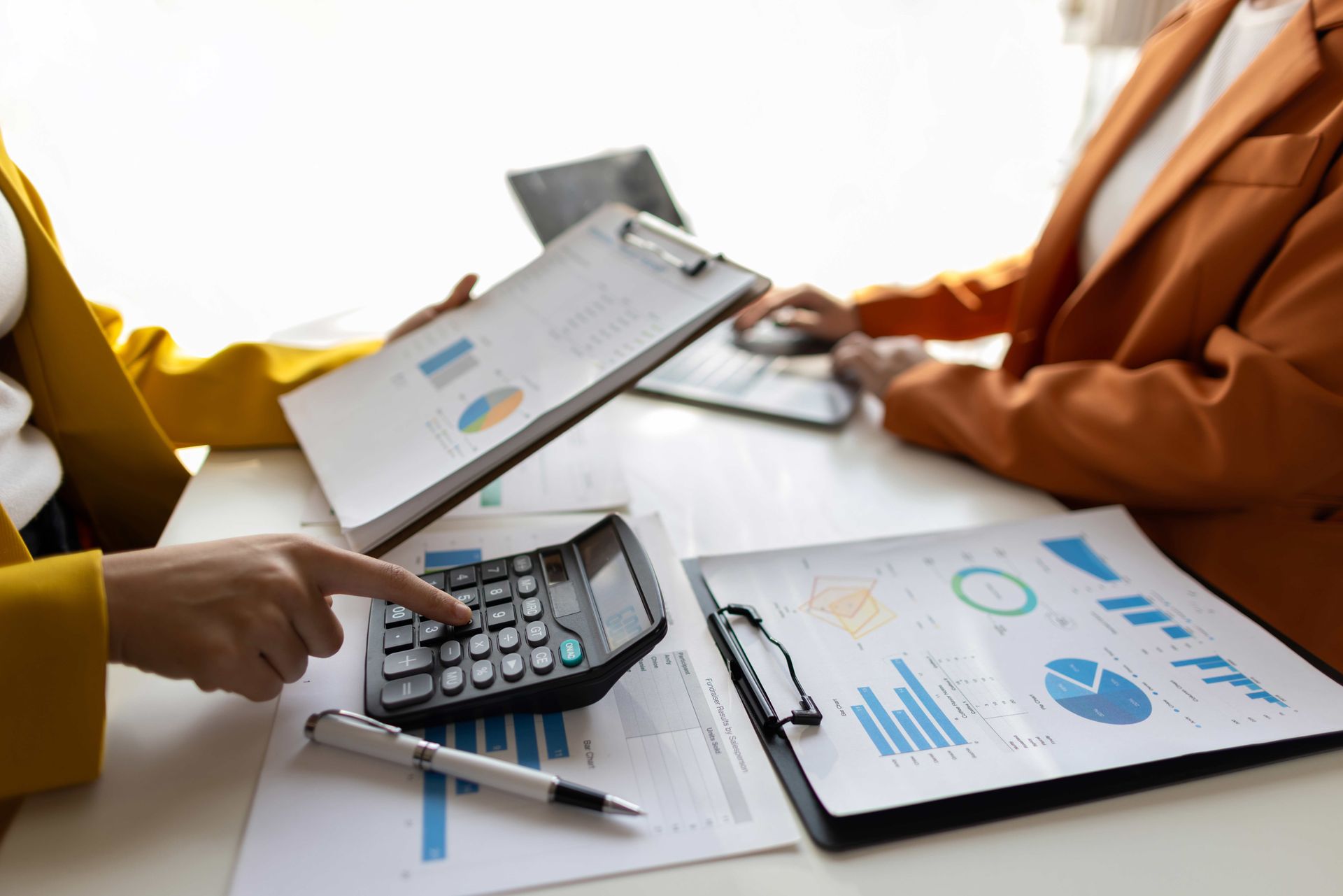 Two people reviewing financial data with a calculator and charts.