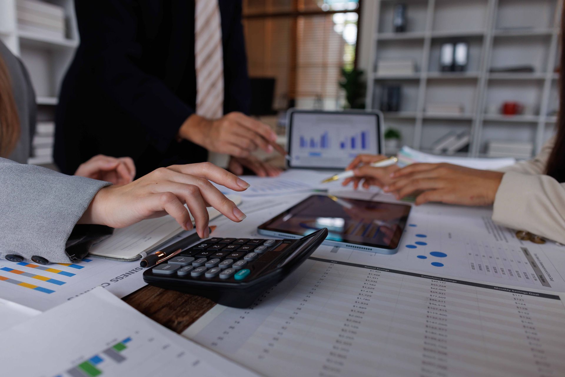People working at a table, using calculators, tablets, and analyzing financial documents.