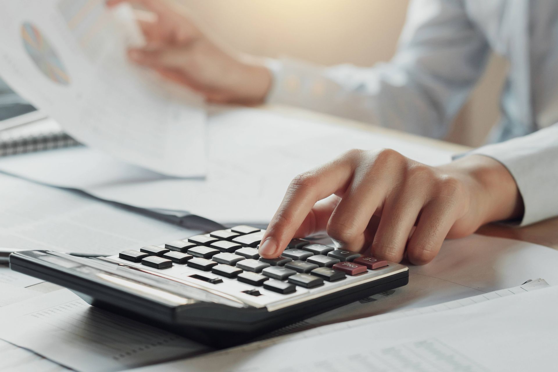 Person calculating with a calculator, reviewing papers at a desk.