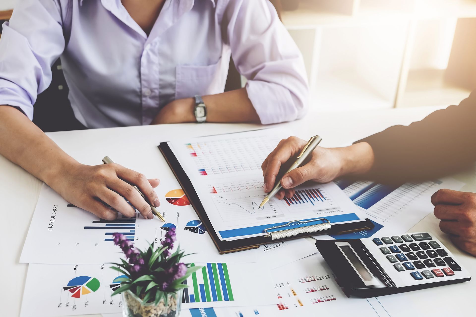 Two people at a table reviewing charts and using a calculator, likely in an office setting.