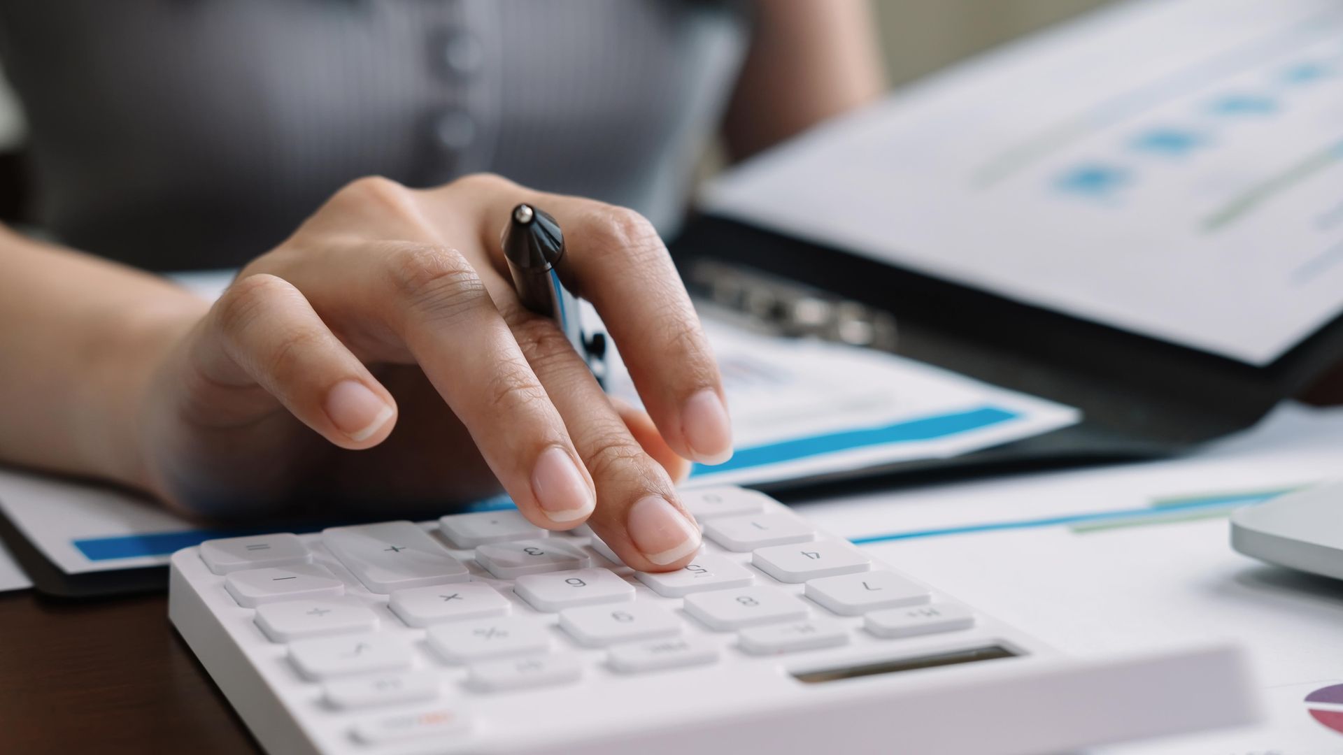 Person's hand using a calculator, with documents and pen nearby, possibly working on finances. Person's hand using a calculator, with documents and pen nearby, possibly working on finances.