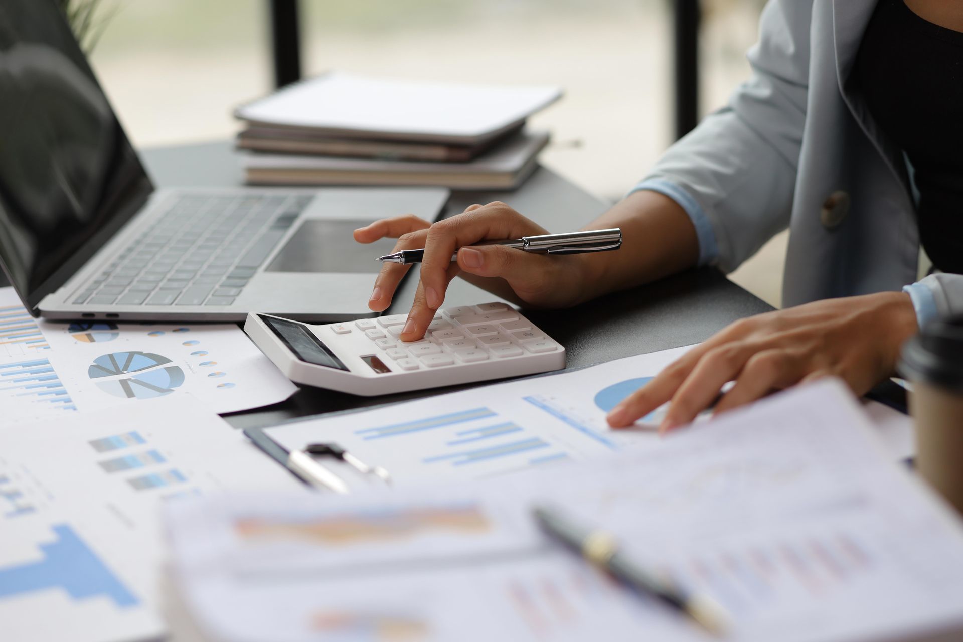 Person using a calculator and laptop, reviewing financial charts and documents on a desk.