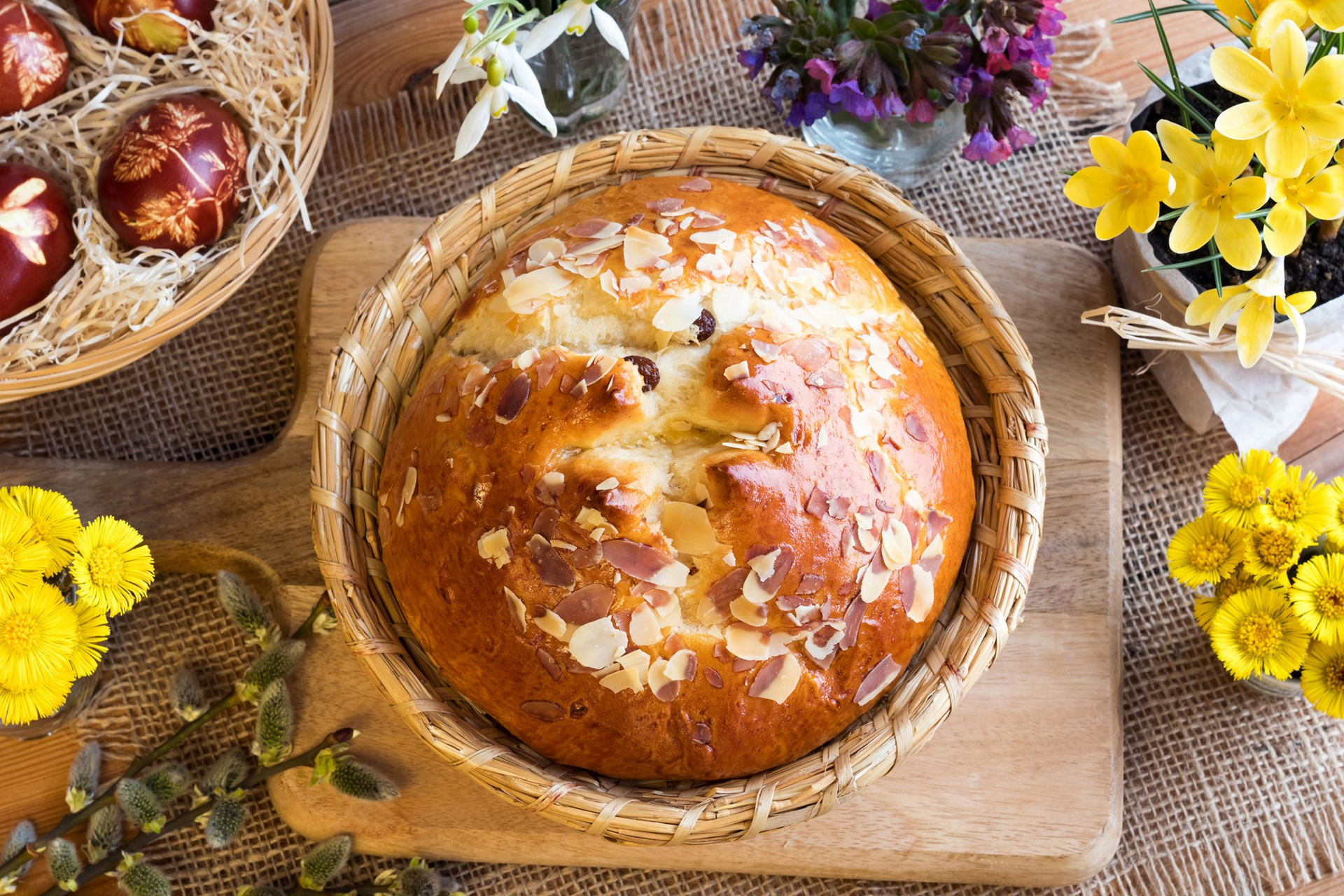 Easter bread with almond topping in a basket, with Easter eggs and flowers.
