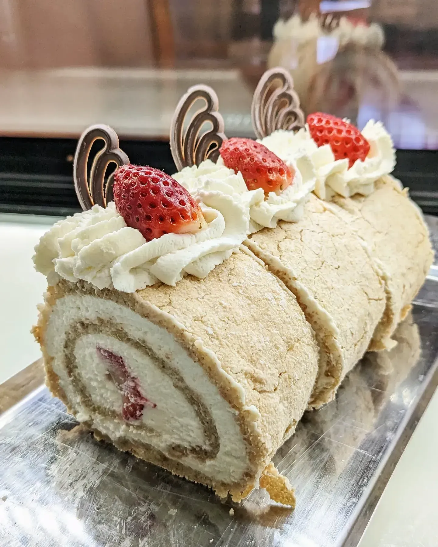 Strawberry-decorated swiss roll cake with cream filling, topped with whipped cream, chocolate swirls, and fresh strawberries.
