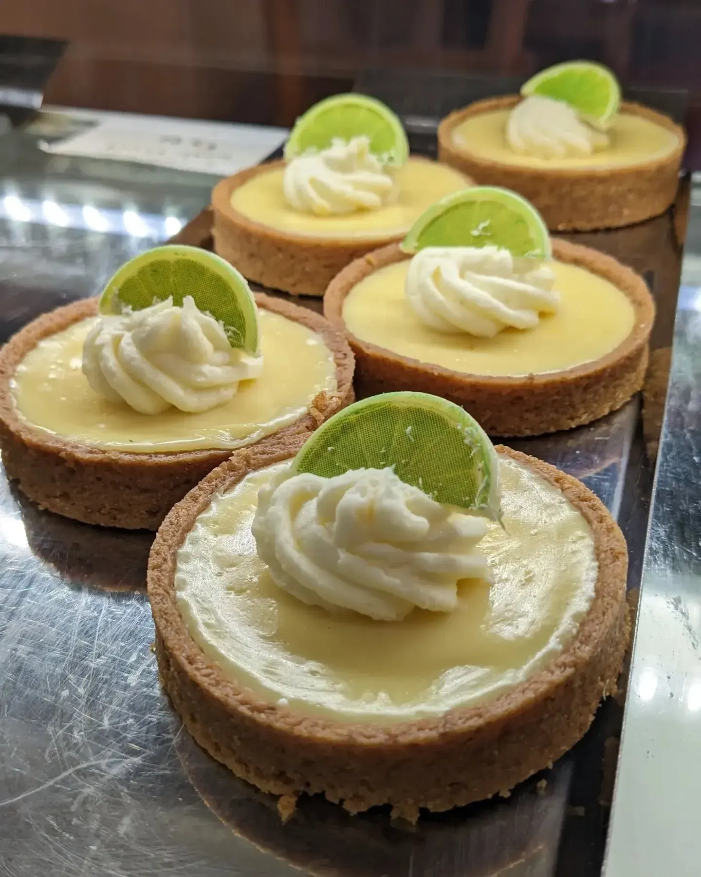Mini lemon tarts with whipped cream topping and lime slice garnish, on display.