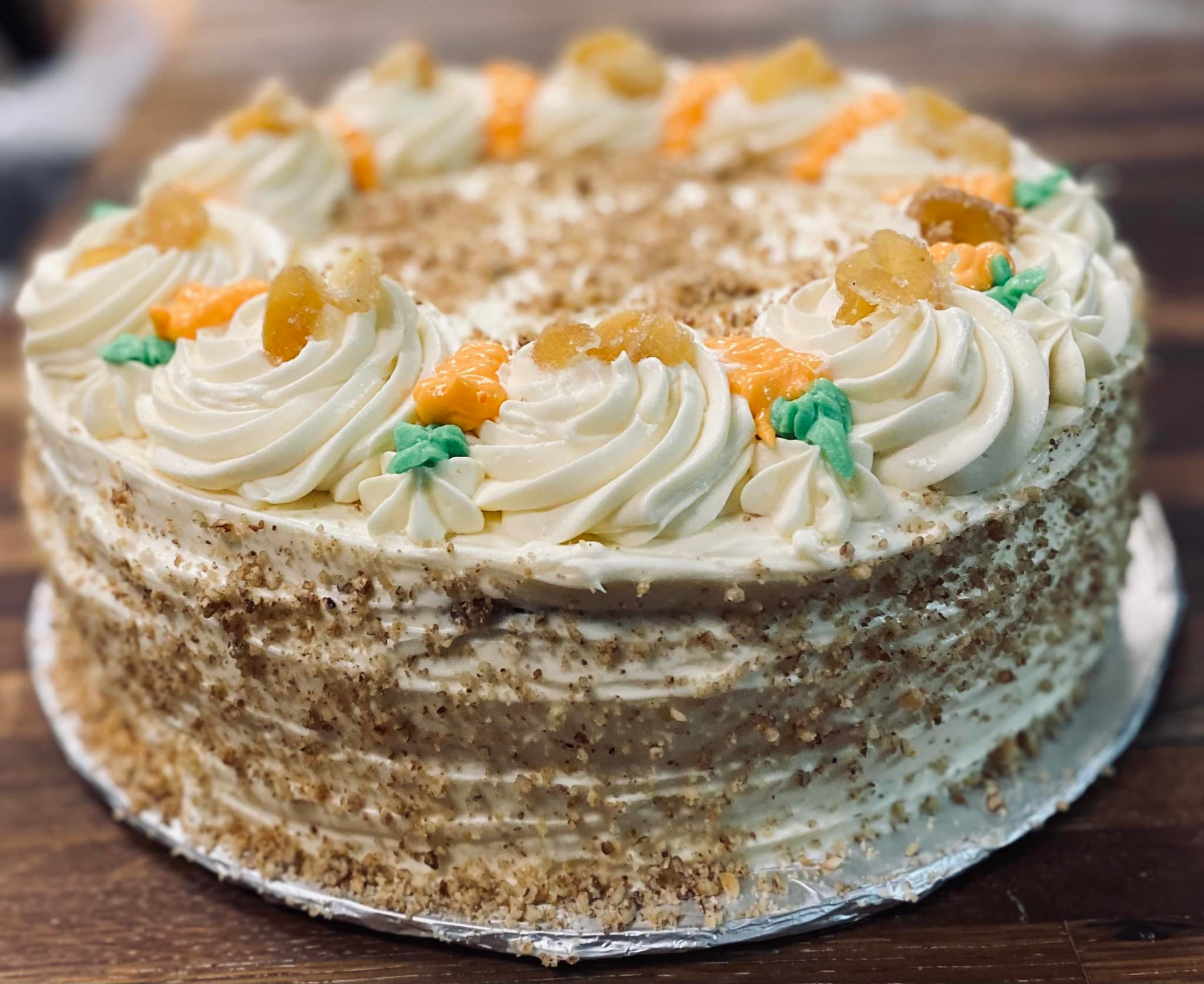Cake with cream frosting, garnished with nuts and candied ginger, on a wooden surface.