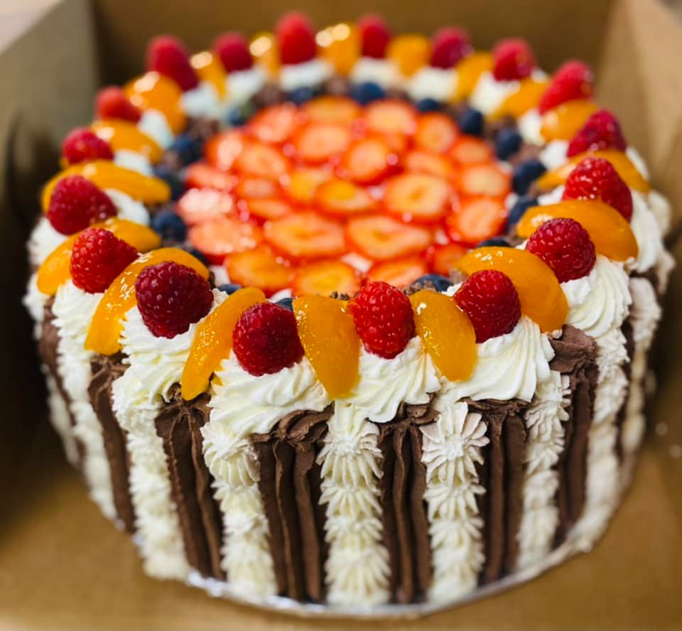 Cake with white and chocolate frosting, topped with fresh fruit: strawberries, blueberries, raspberries, and peaches.