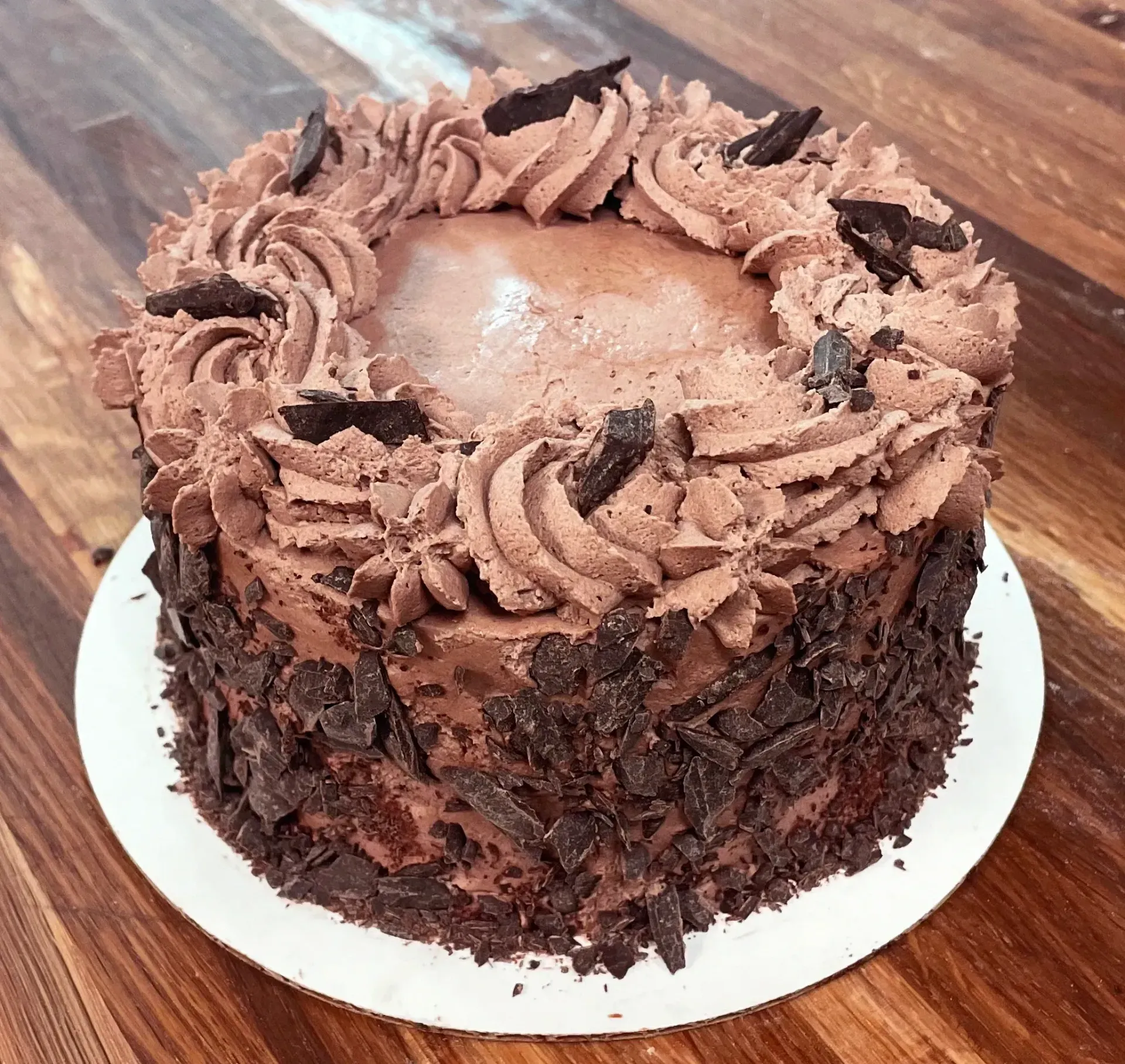 Chocolate cake with chocolate frosting, garnished with chocolate shavings, on a white plate.
