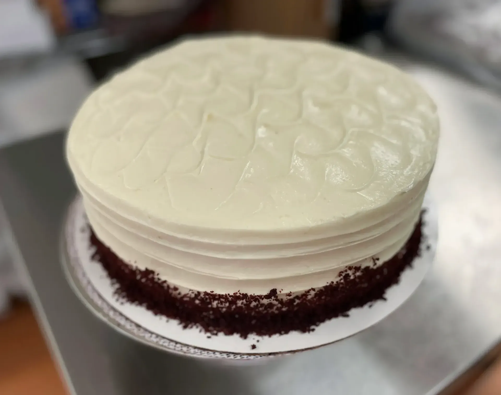 Red velvet cake with white frosting and red crumbs on a silver cake stand.