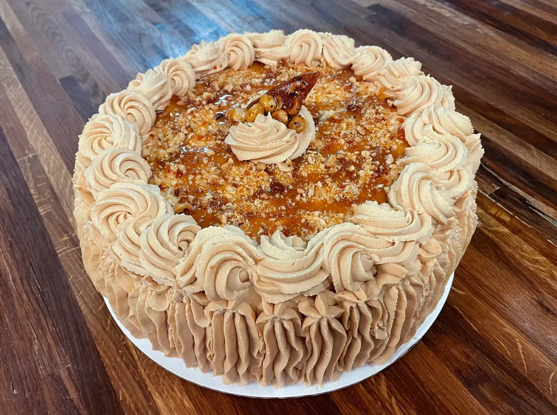 Cake with tan frosting and caramel topping, on a wooden table.