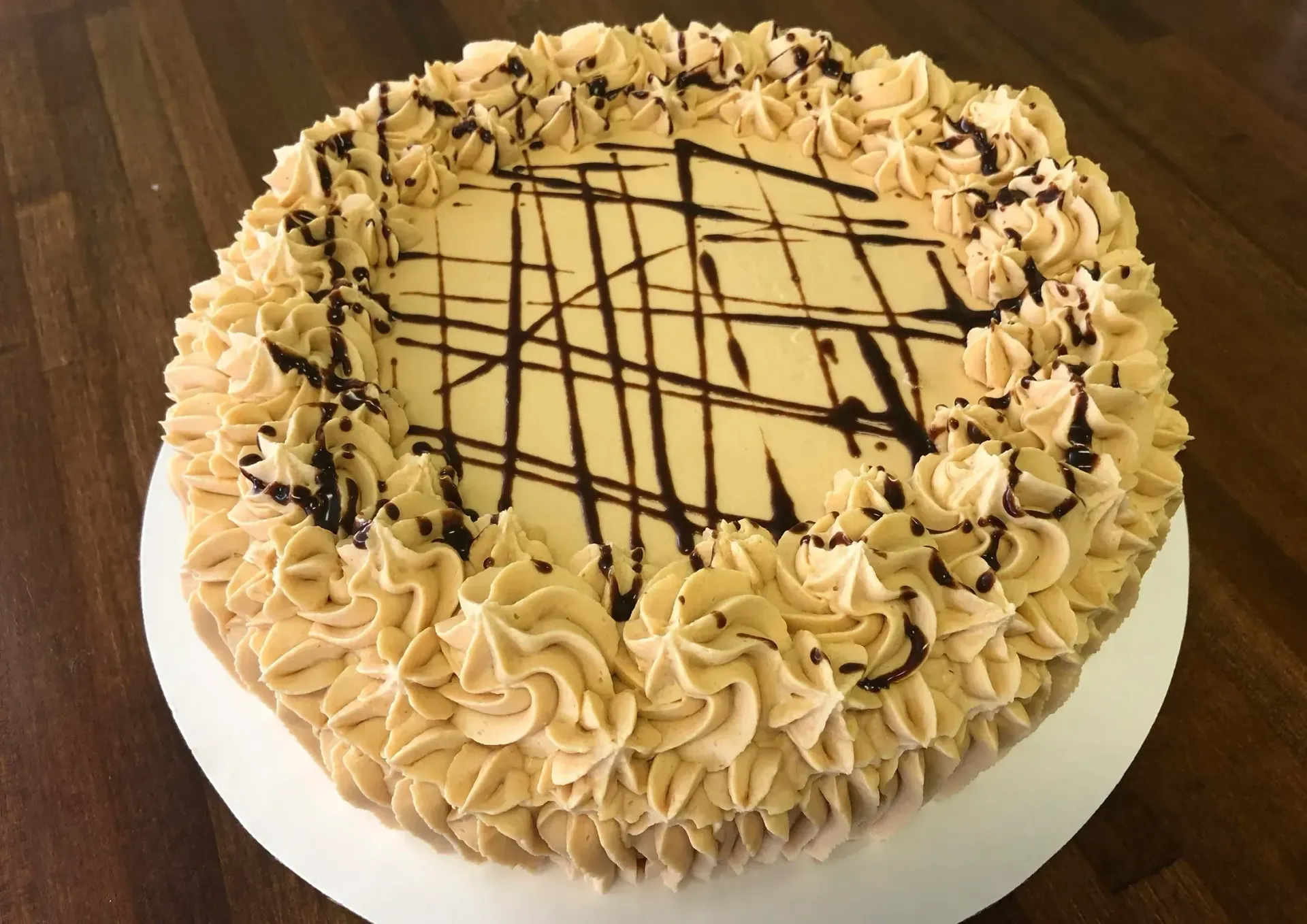 Cake with light brown frosting and chocolate drizzle, decorated with rosettes around the edge.