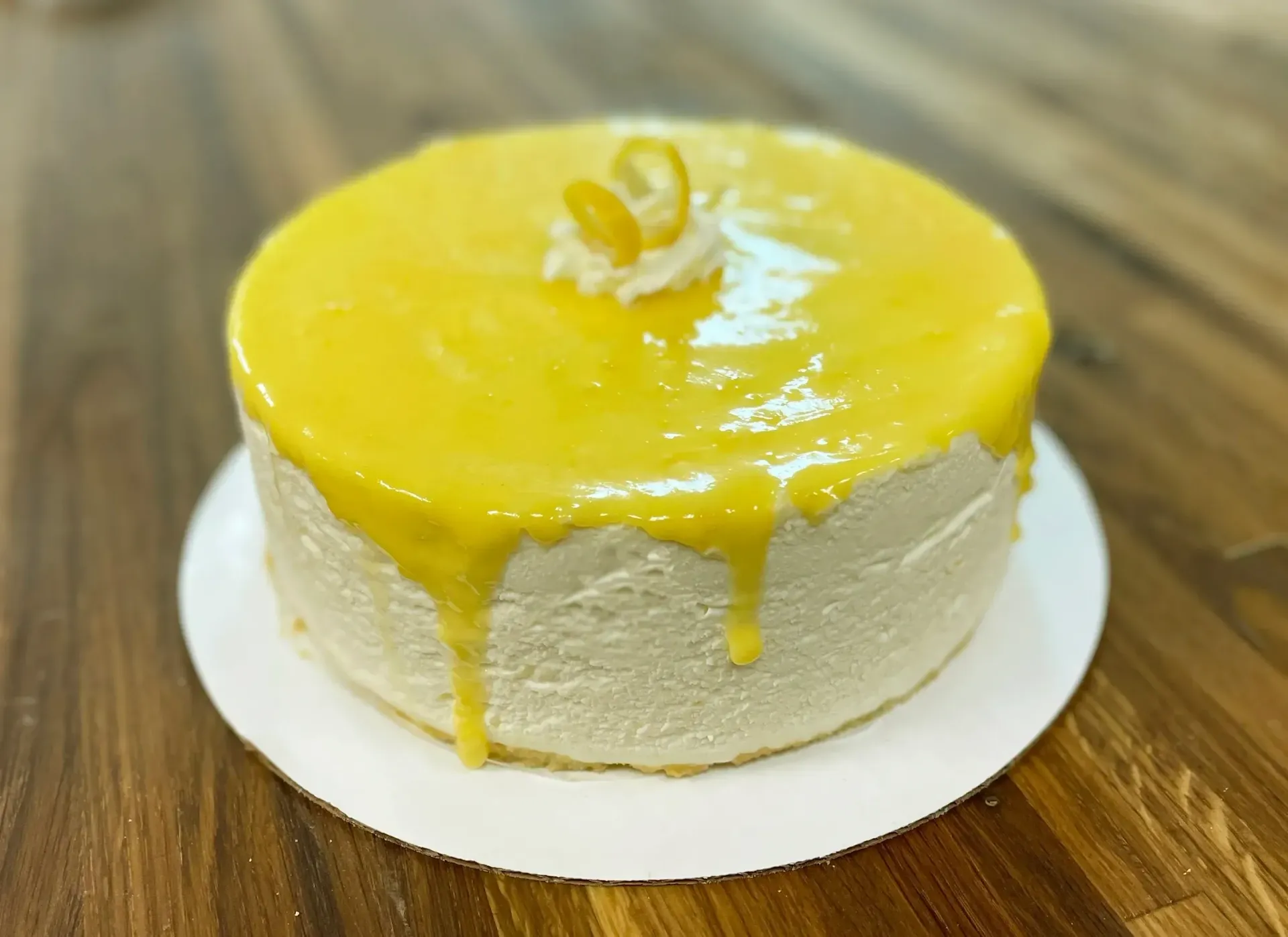 Lemon cake with yellow glaze on white plate, wooden table.