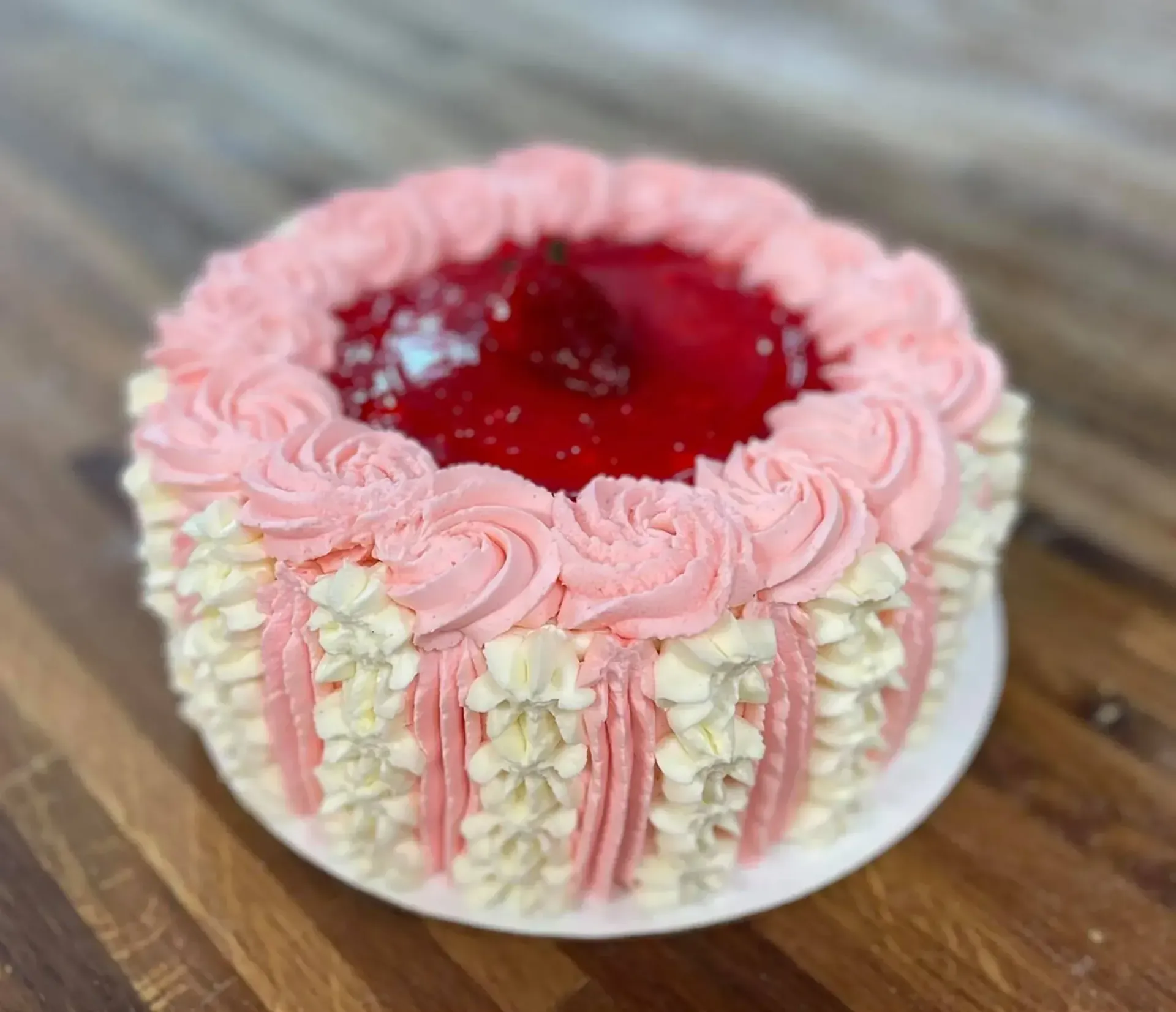 Strawberry shortcake with pink and white frosting on a wooden table.