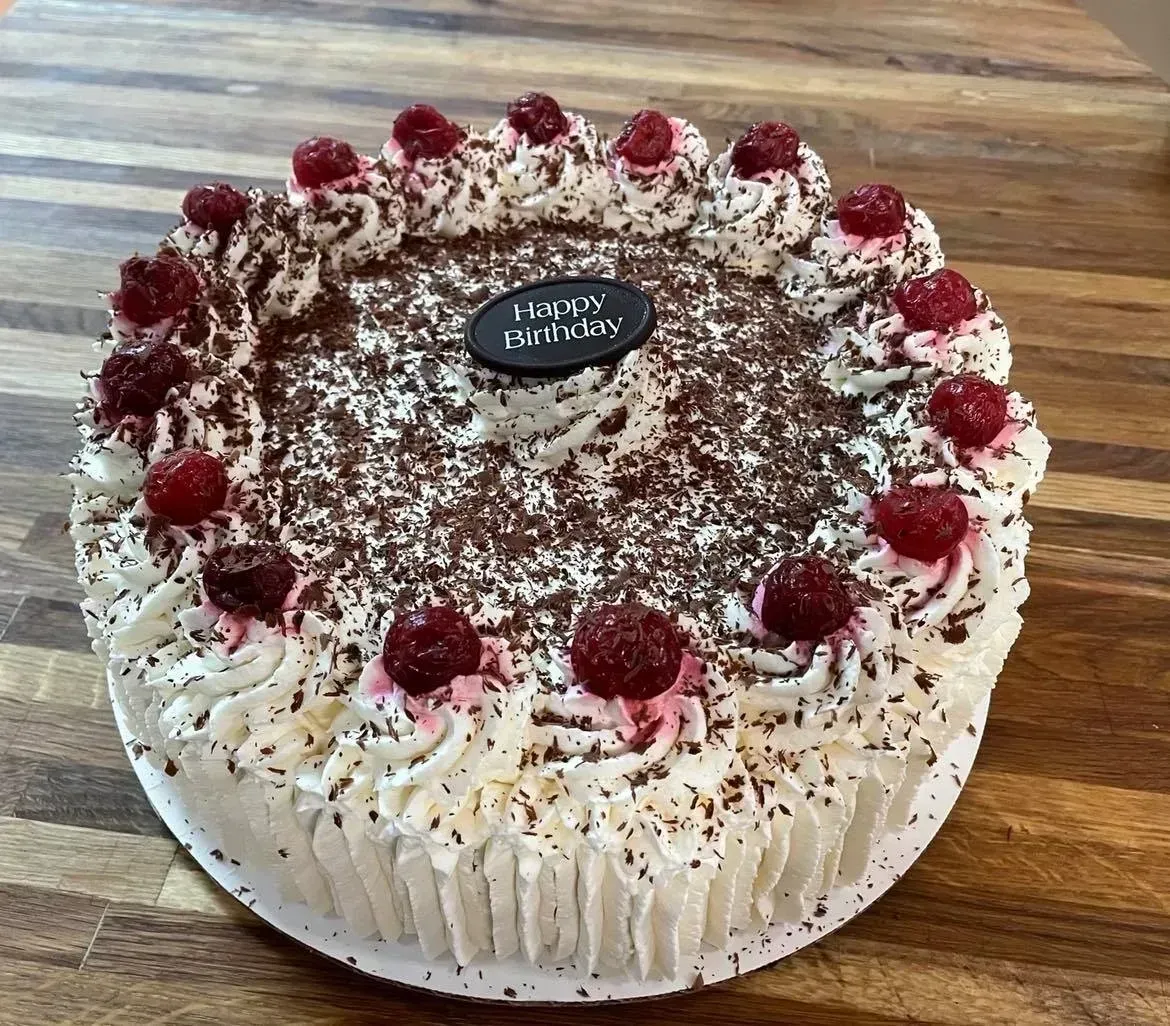 Black Forest cake with whipped cream, cherries, and chocolate shavings on a wooden surface.
