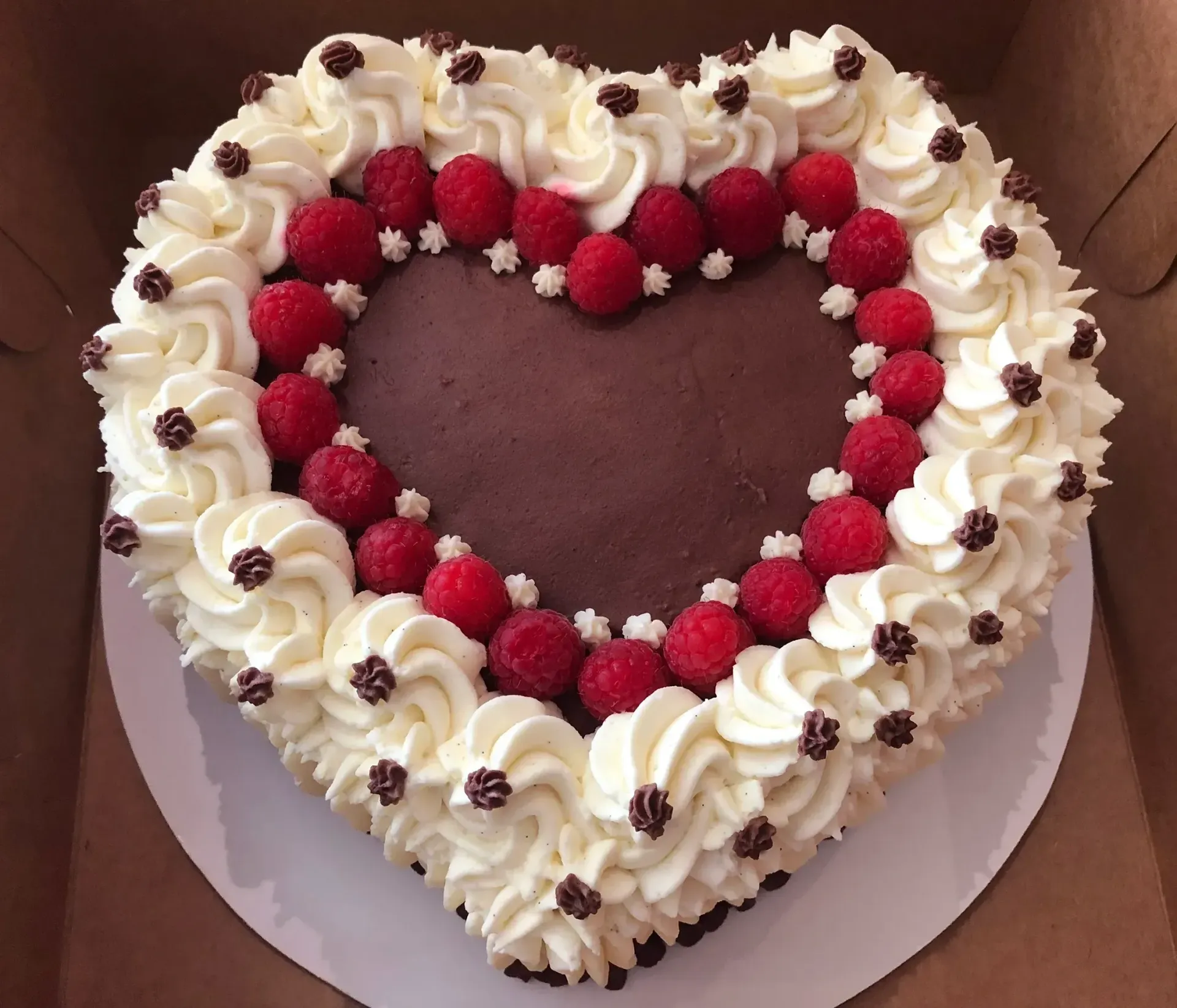 Heart-shaped cake with whipped cream frosting, raspberries, and chocolate sprinkles.