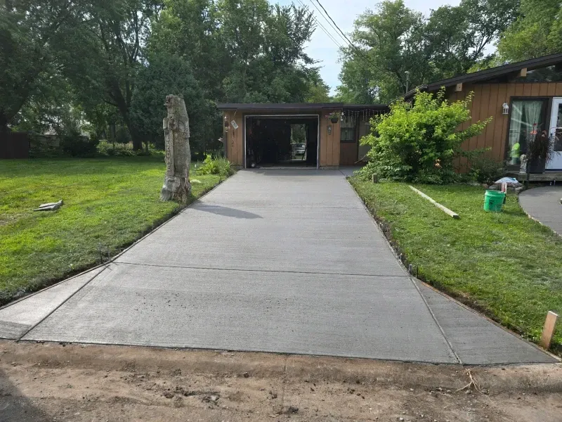 Newly poured concrete driveway leading to a garage, flanked by green grass. A house is in the background.