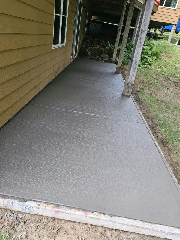 Newly poured concrete walkway next to a light yellow house with a white framed window.