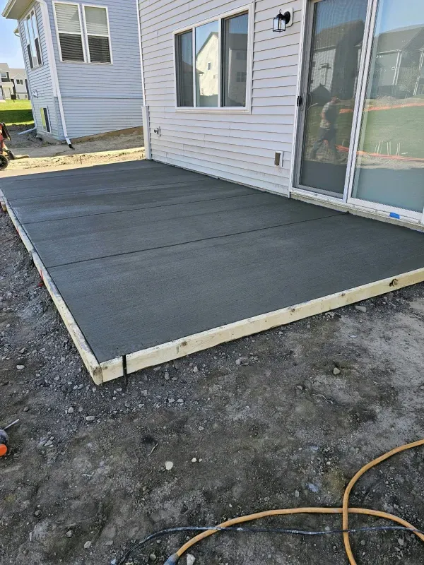 Newly poured concrete patio next to a house with a sliding glass door.