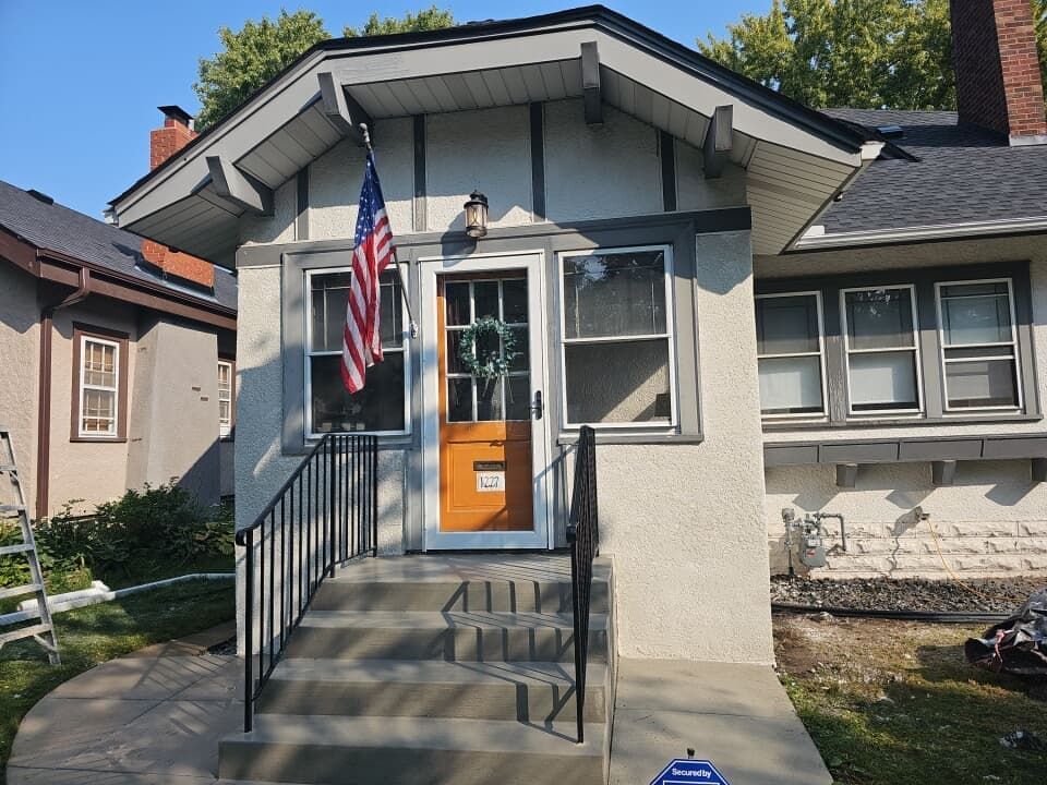 House exterior with American flag hanging on the front porch. Orange door, black railing, and gray trim.