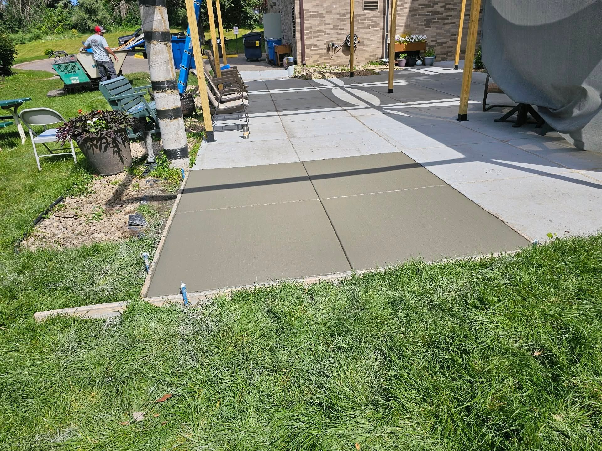 Freshly poured concrete patio section next to existing patio, with grass and building in the background.