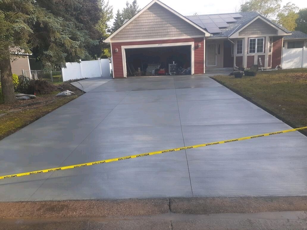 Newly poured gray concrete driveway in front of a house, caution tape across it.