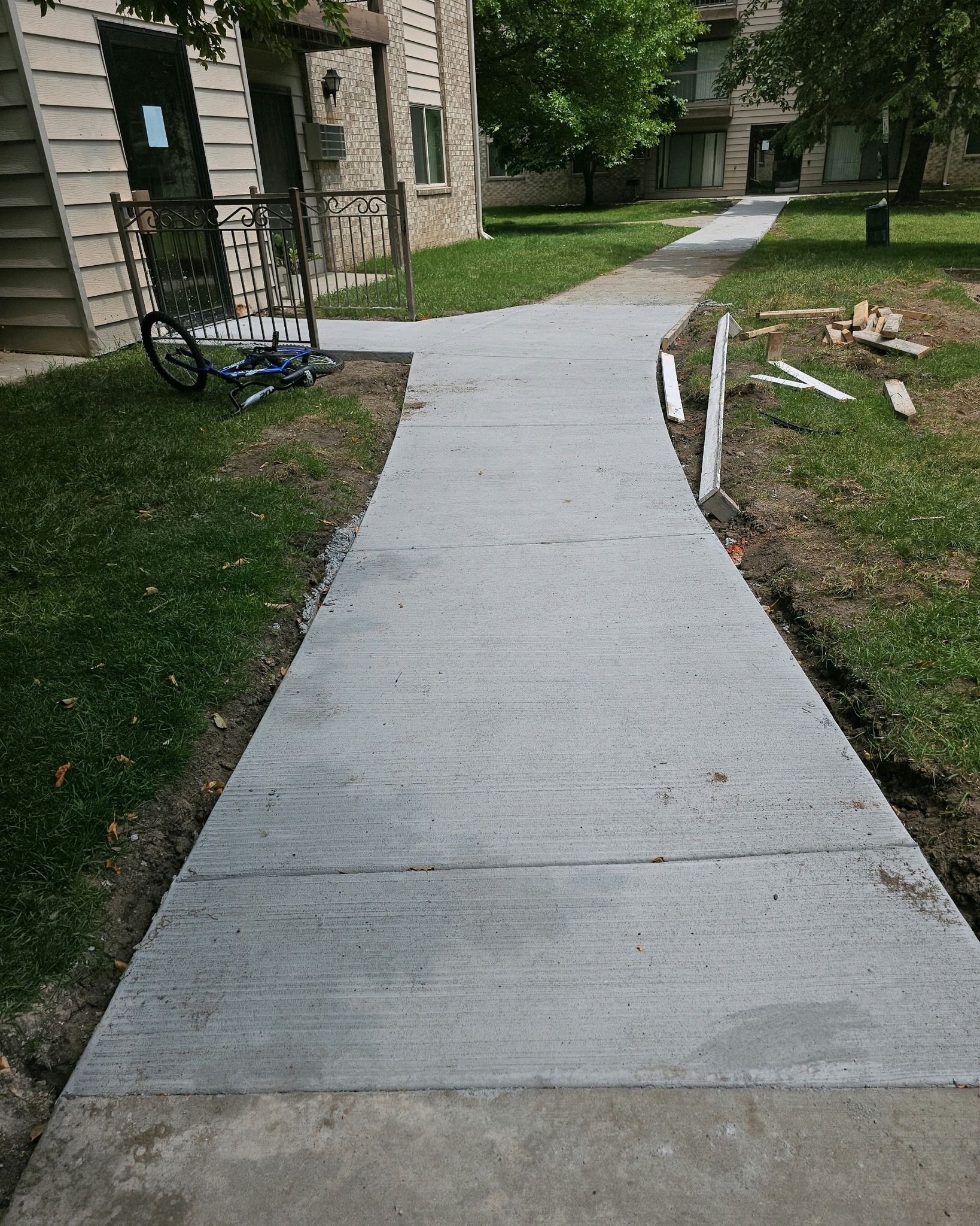Newly poured concrete sidewalk leading through a grassy area, alongside a building.